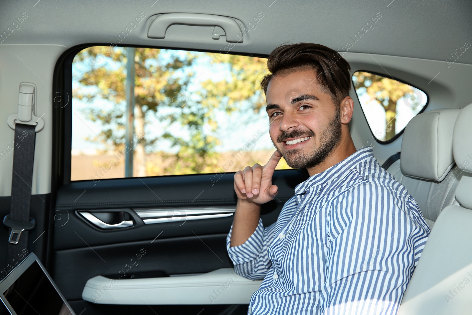 Photo of Young handsome man with laptop in back seat of car