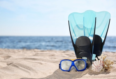 Photo of Diving mask, flippers and seashells on sand near sea, space for text. Beach objects