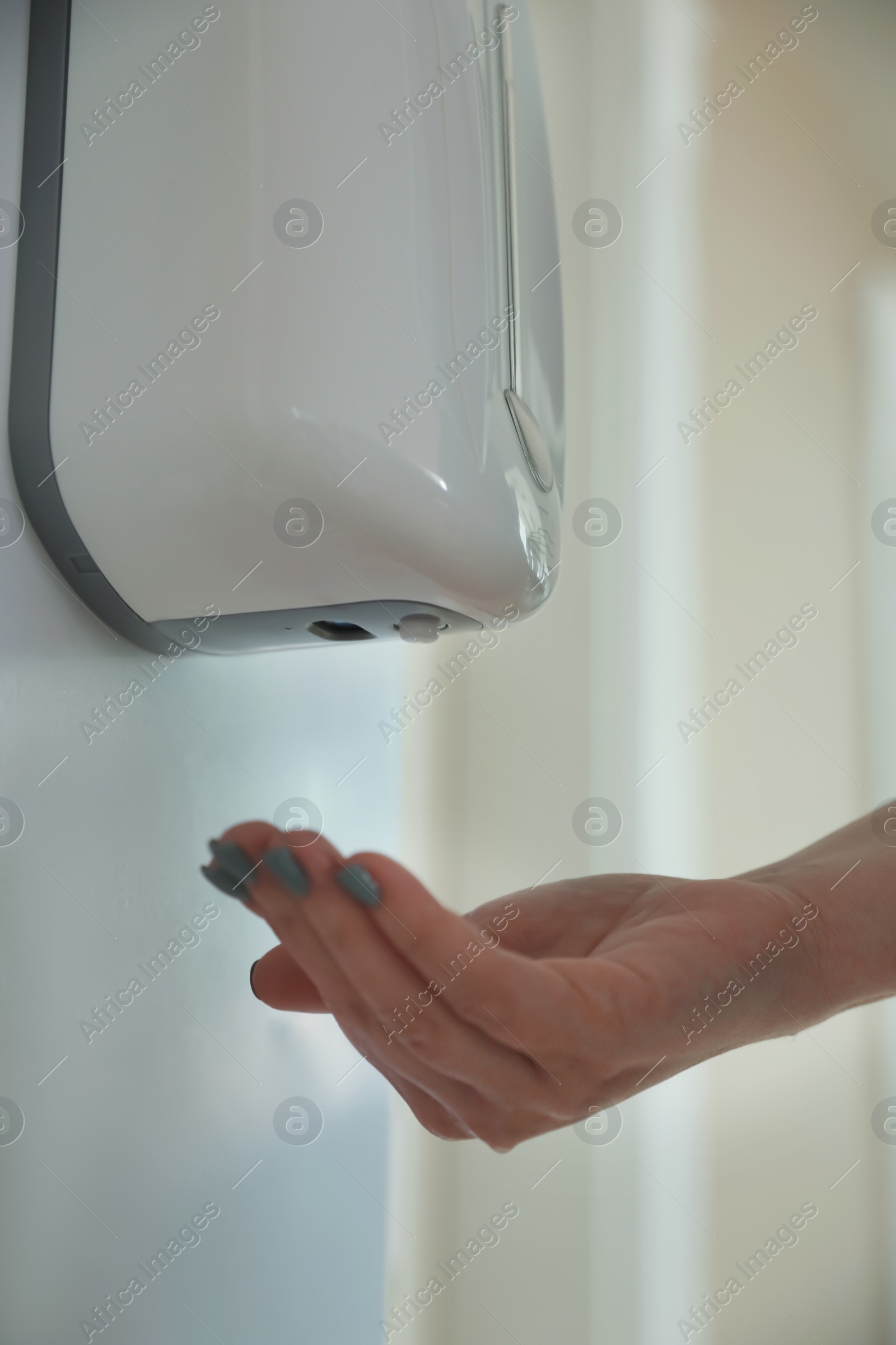 Photo of Woman using automatic hand sanitizer dispenser indoors, closeup