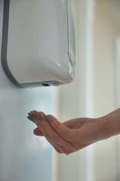 Woman using automatic hand sanitizer dispenser indoors, closeup
