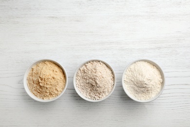 Photo of Bowls with different types of flour on white wooden background, top view. Space for text