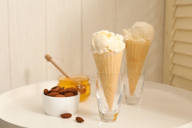 Photo of Delicious vanilla ice cream in wafer cones with honey and almonds on white table indoors