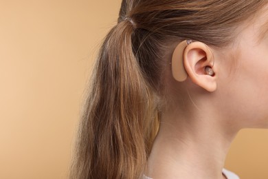 Photo of Little girl with hearing aid on pale brown background, closeup. Space for text