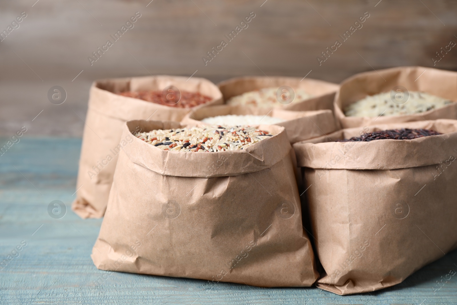 Photo of Brown and polished rice in paper bags on blue wooden table