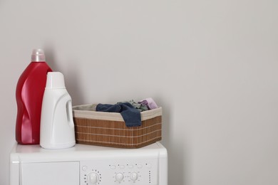 Photo of Baby clothes in wicker basket and laundry detergents on washing machine near light wall, space for text