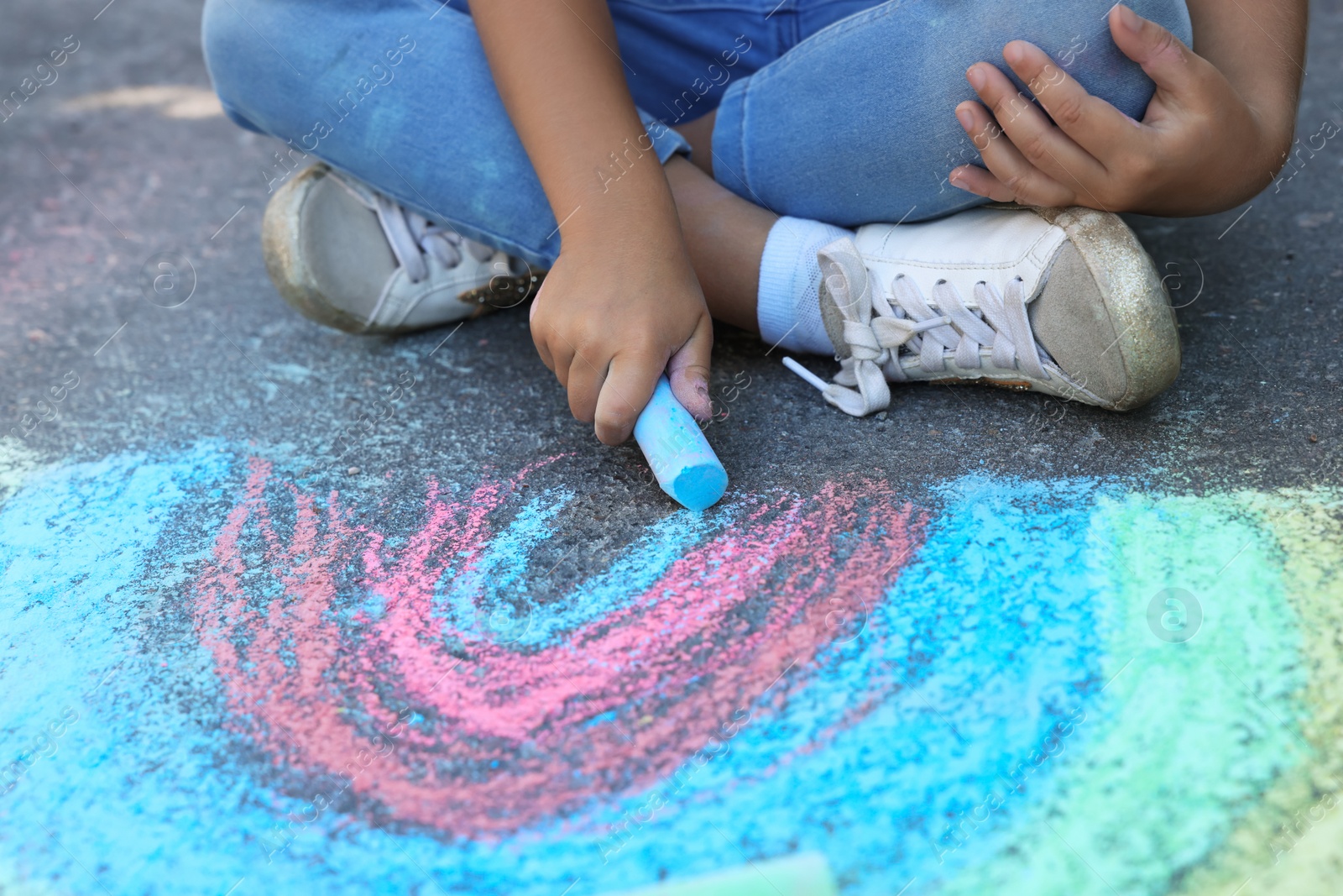 Photo of Little child drawing rainbow with colorful chalk on asphalt, closeup