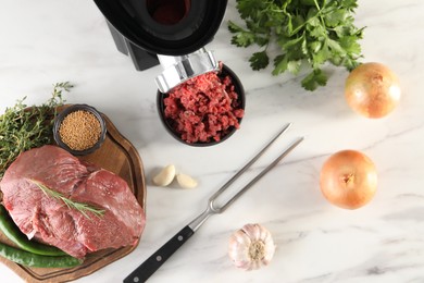 Electric meat grinder with beef mince and products on white marble table in kitchen, flat lay