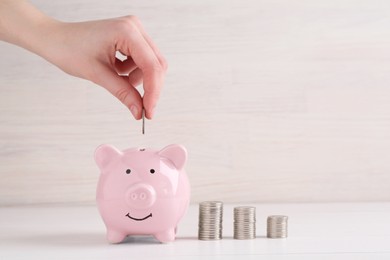 Financial savings. Woman putting coin into piggy bank at white wooden table, closeup