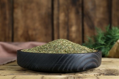 Dried dill in bowl on wooden table, closeup