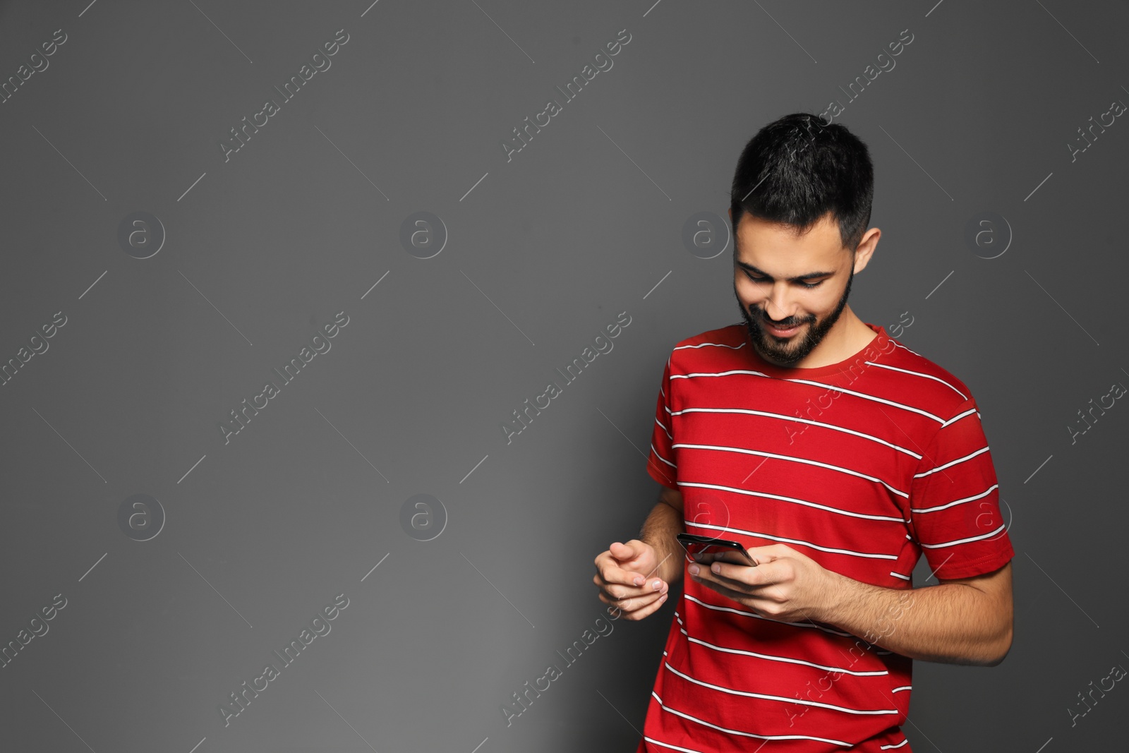 Photo of Portrait of handsome young man with mobile phone on gray background. Space for text