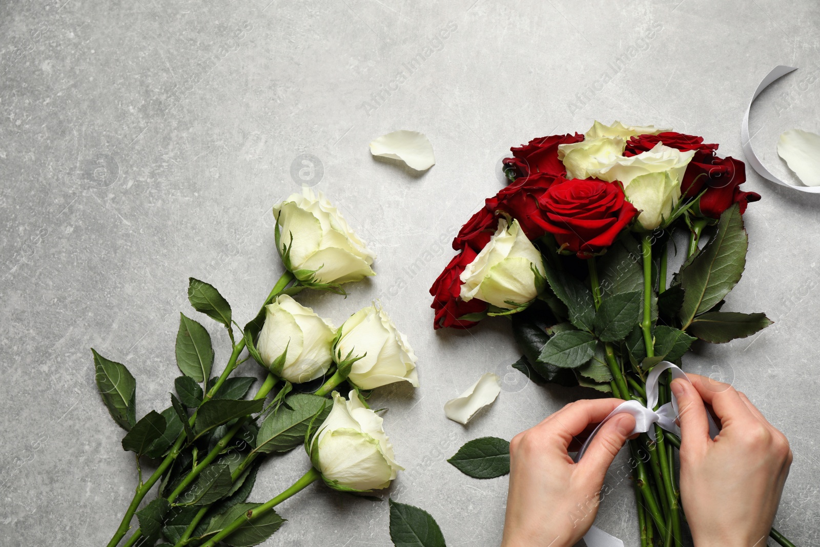 Photo of Woman making luxury bouquet of fresh roses at grey table, top view