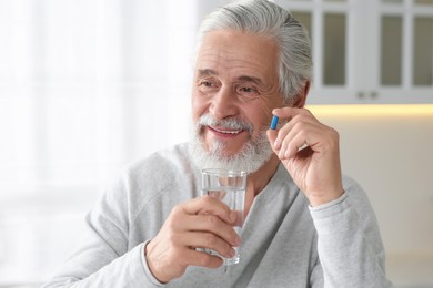 Senior man with glass of water and pill indoors