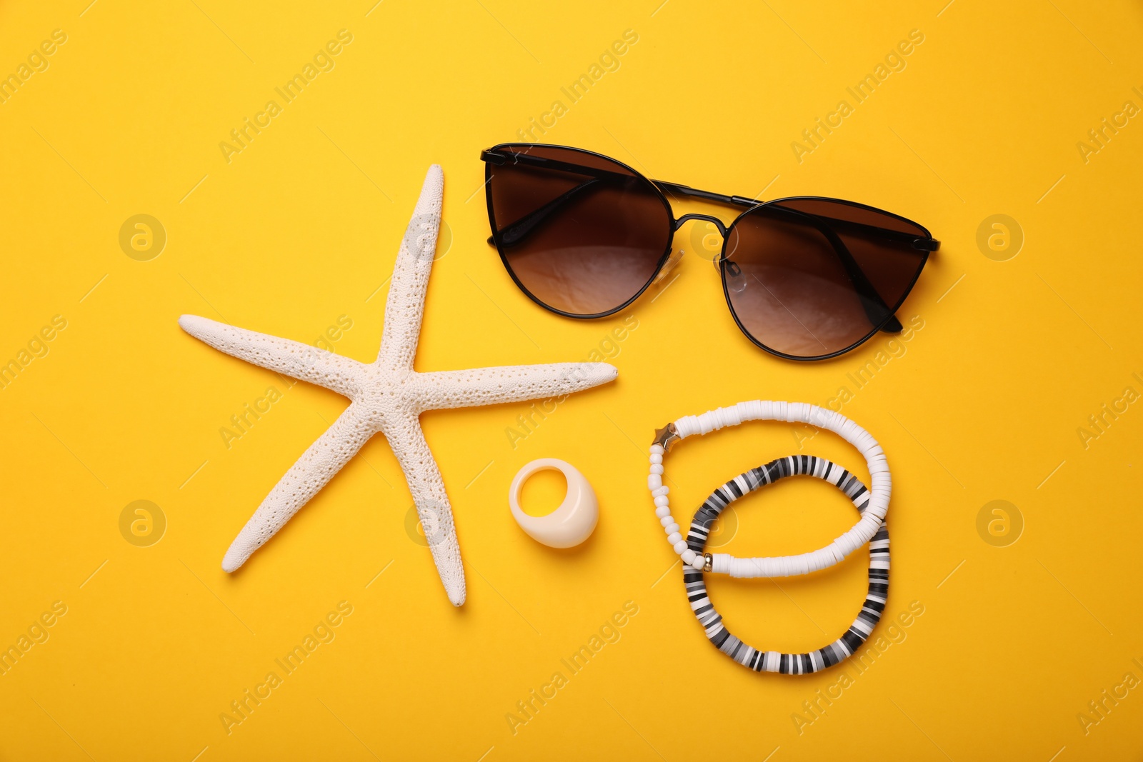 Photo of Stylish sunglasses, bracelets, ring and starfish on yellow background, flat lay