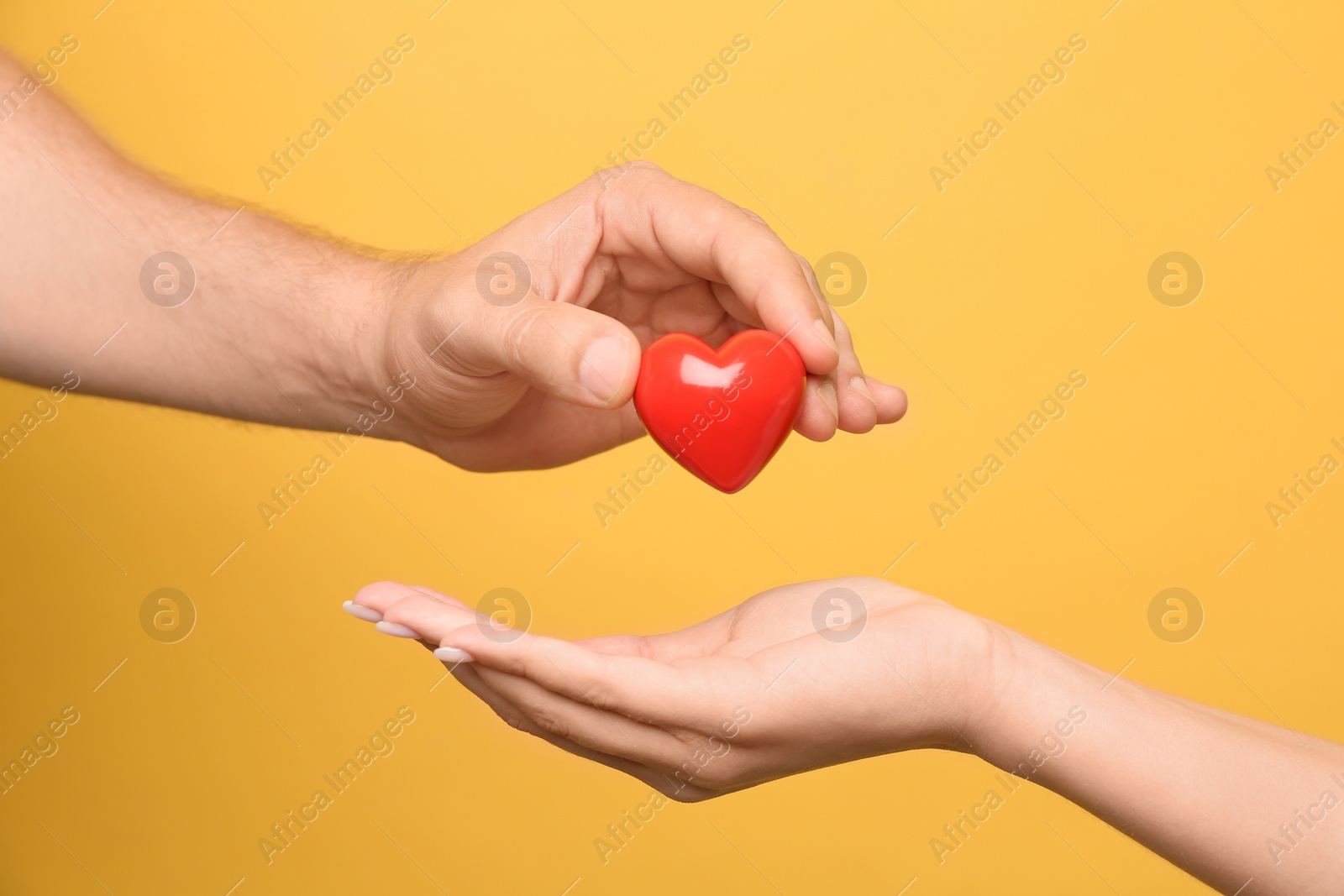 Photo of Man giving red heart to woman on yellow background, closeup. Donation concept