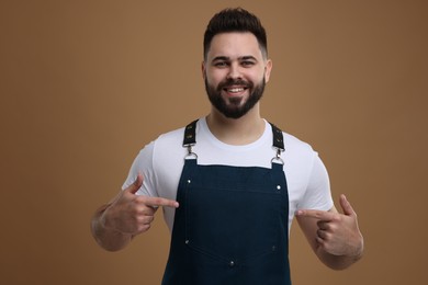 Photo of Smiling man pointing at kitchen apron on brown background. Mockup for design