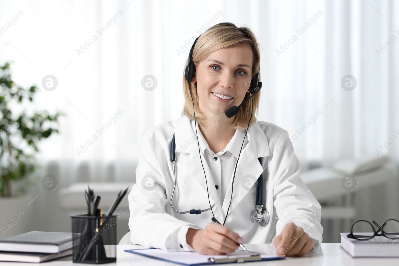 Photo of Smiling doctor in headphones having online consultation at table indoors