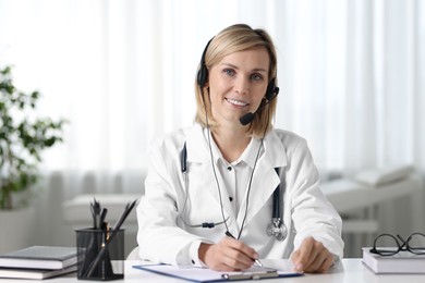 Smiling doctor in headphones having online consultation at table indoors