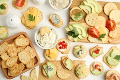 Different snacks with salted crackers on white wooden table, flat lay