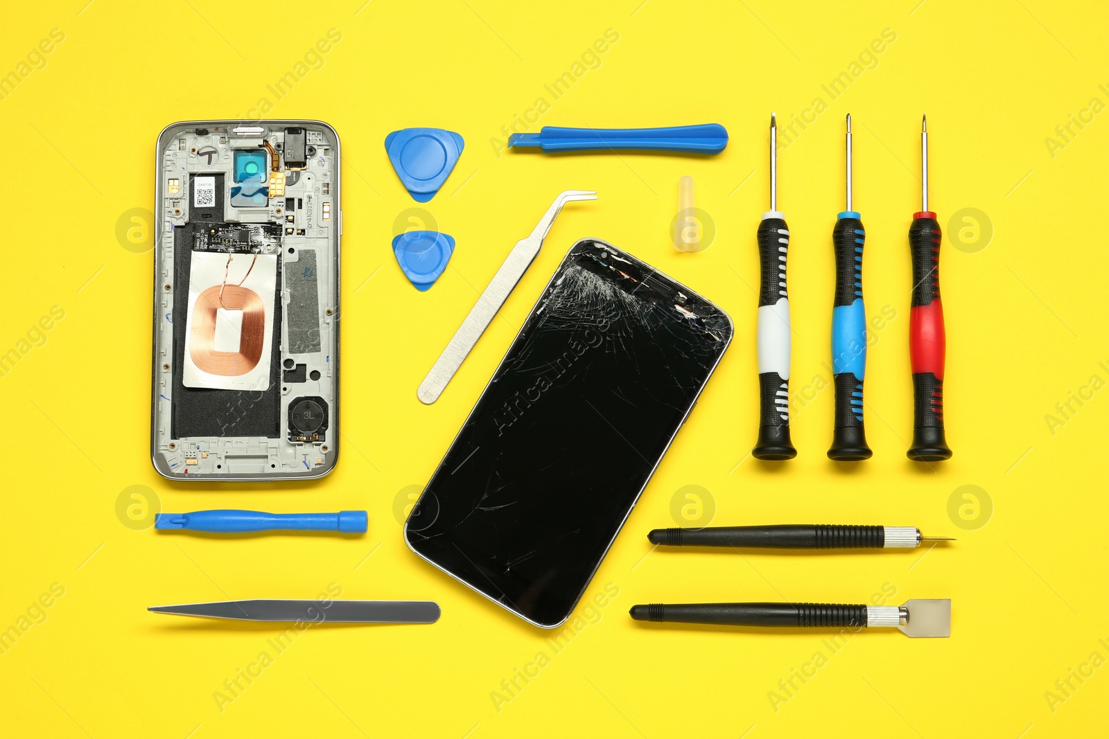 Photo of Damaged smartphone and repair tool set on yellow background, flat lay