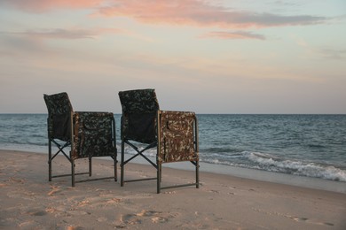 Photo of Camping chairs on sandy beach near sea, space for text
