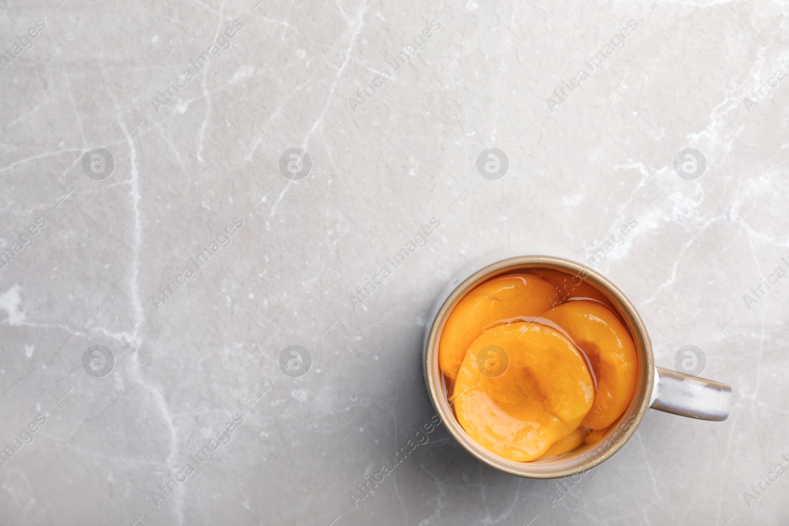 Photo of Cup with conserved peach halves on grey background, top view. Space for text