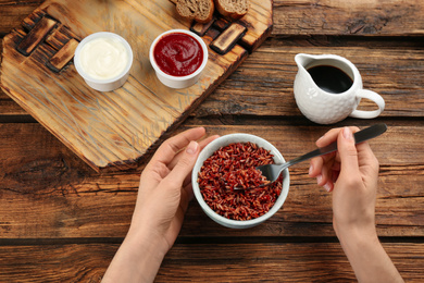 Photo of Woman eating tasty brown rice at wooden table, top view