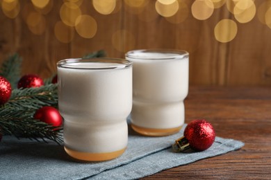 Photo of Glasses of delicious eggnog and decorated fir branch on wooden table, space for text