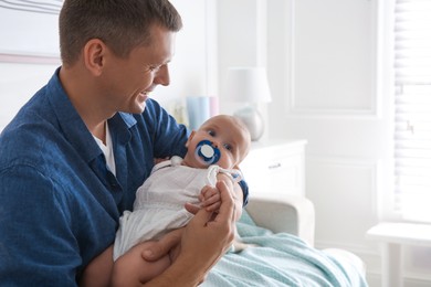 Happy father holding his cute little baby with pacifier at home, space for text