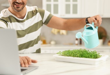 Photo of Teacher with microgreens and watering can conducting online course in kitchen, closeup. Time for hobby