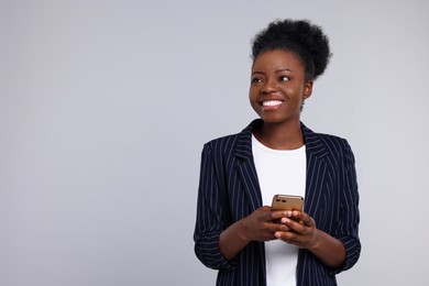 Happy young woman with smartphone on light grey background