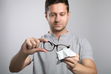 Photo of Man wiping glasses with microfiber cloth on light grey background
