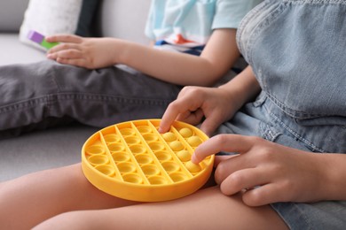 Photo of Little children playing with pop it fidget toys on sofa, closeup