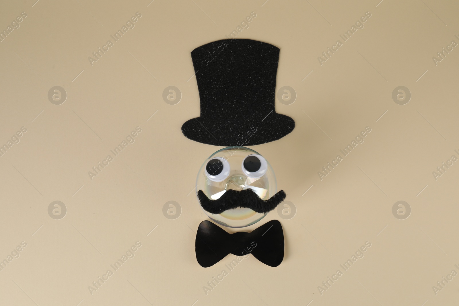 Photo of Man's face made of fake mustache, ball, hat, bow tie and eyes on beige background, top view