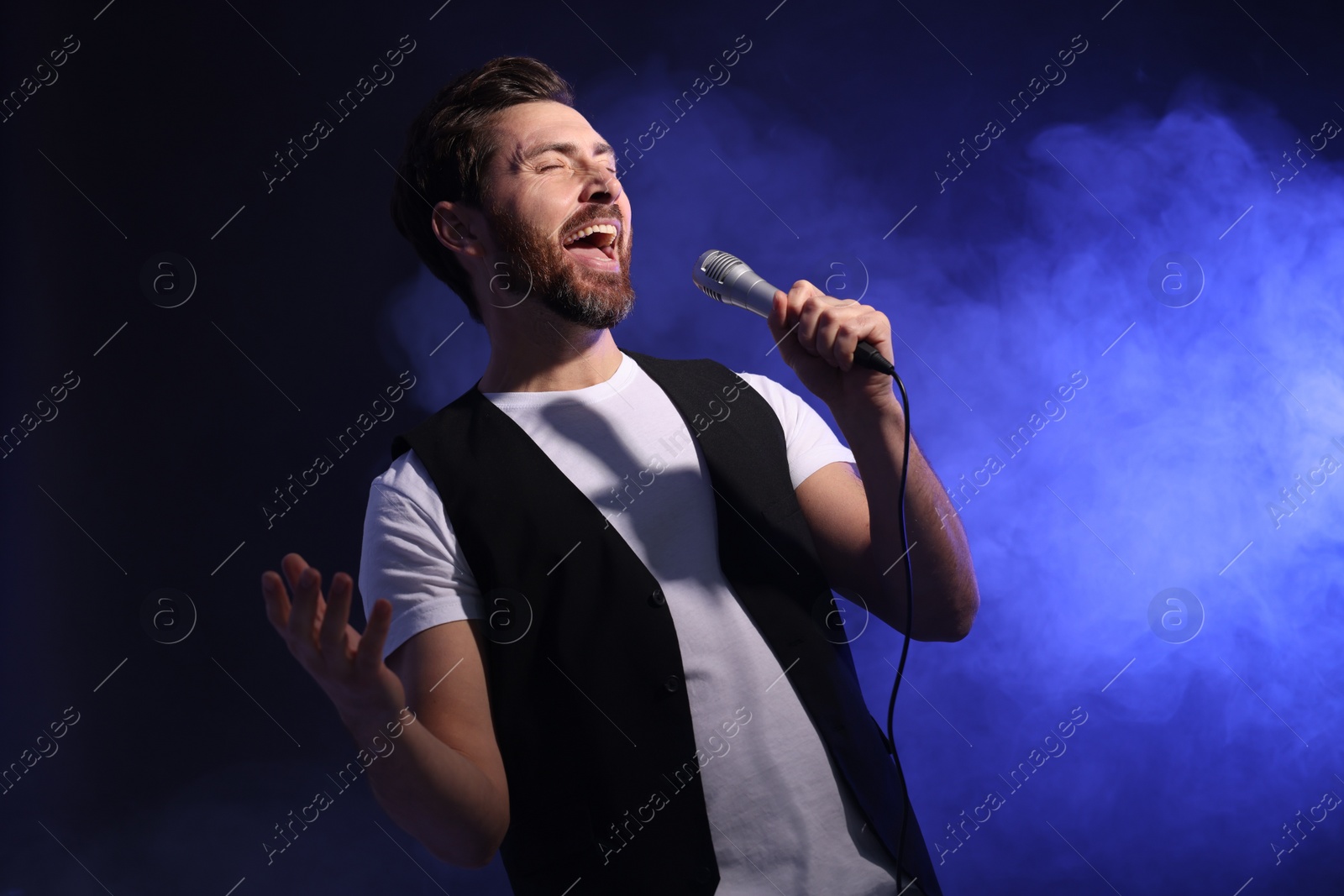 Photo of Handsome man with microphone singing on dark blue background