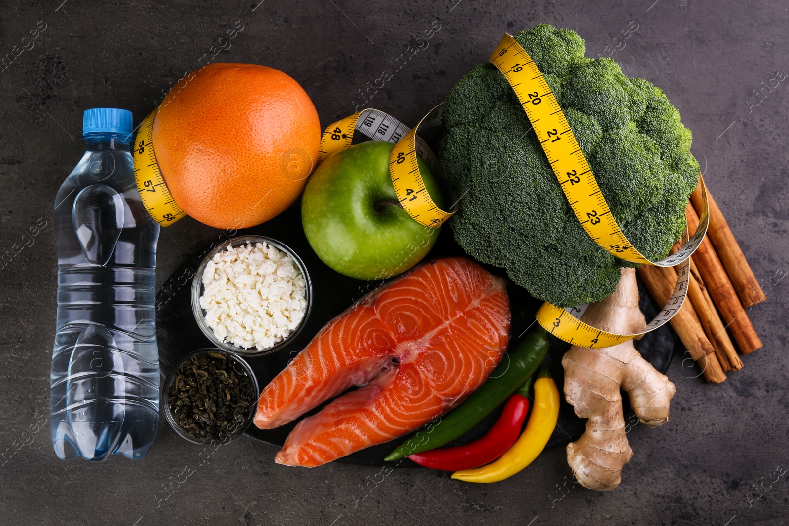 Photo of Metabolism. Different food products and measuring tape on grey table, flat lay