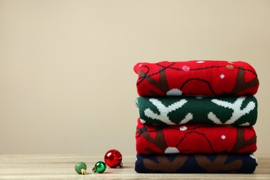 Photo of Stack of different Christmas sweaters and baubles on wooden table against beige background, space for text