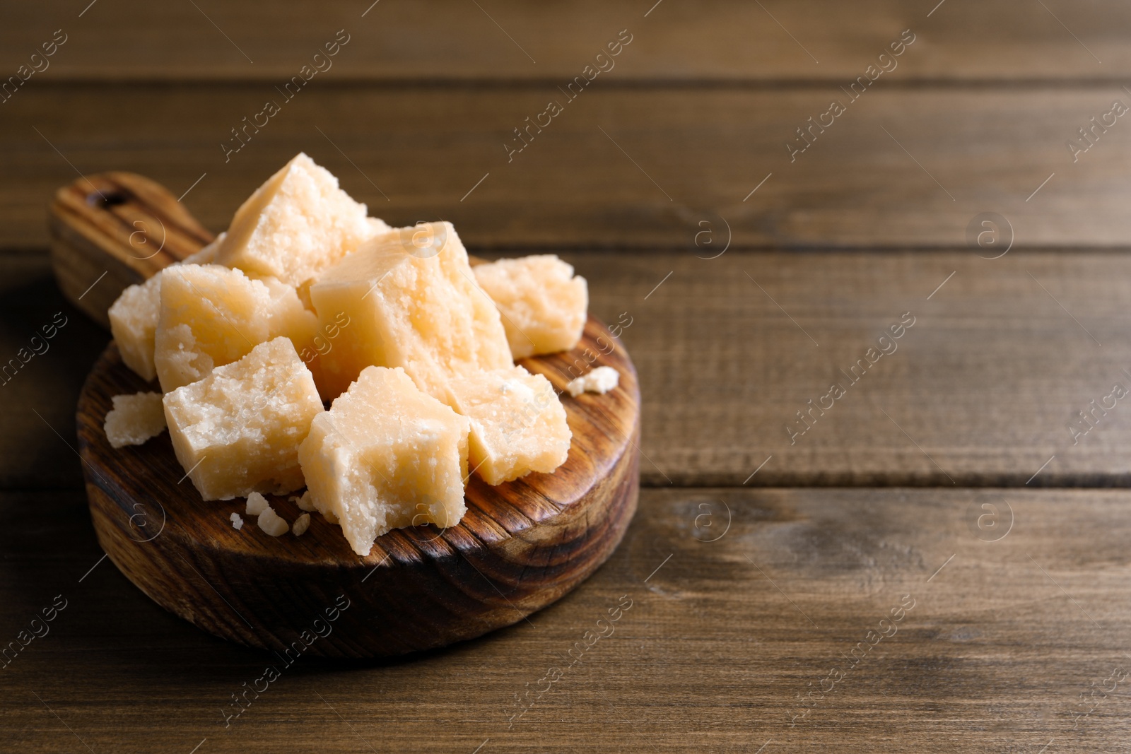 Photo of Pieces of delicious parmesan cheese on wooden table. Space for text
