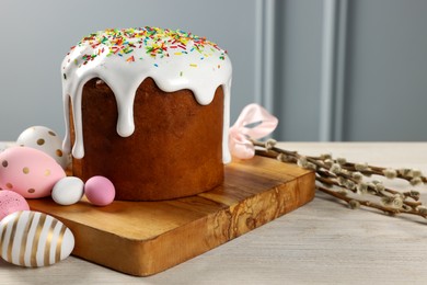 Photo of Delicious Easter cake with sprinkles, decorated eggs and willow branches on white wooden table near light grey wall indoors