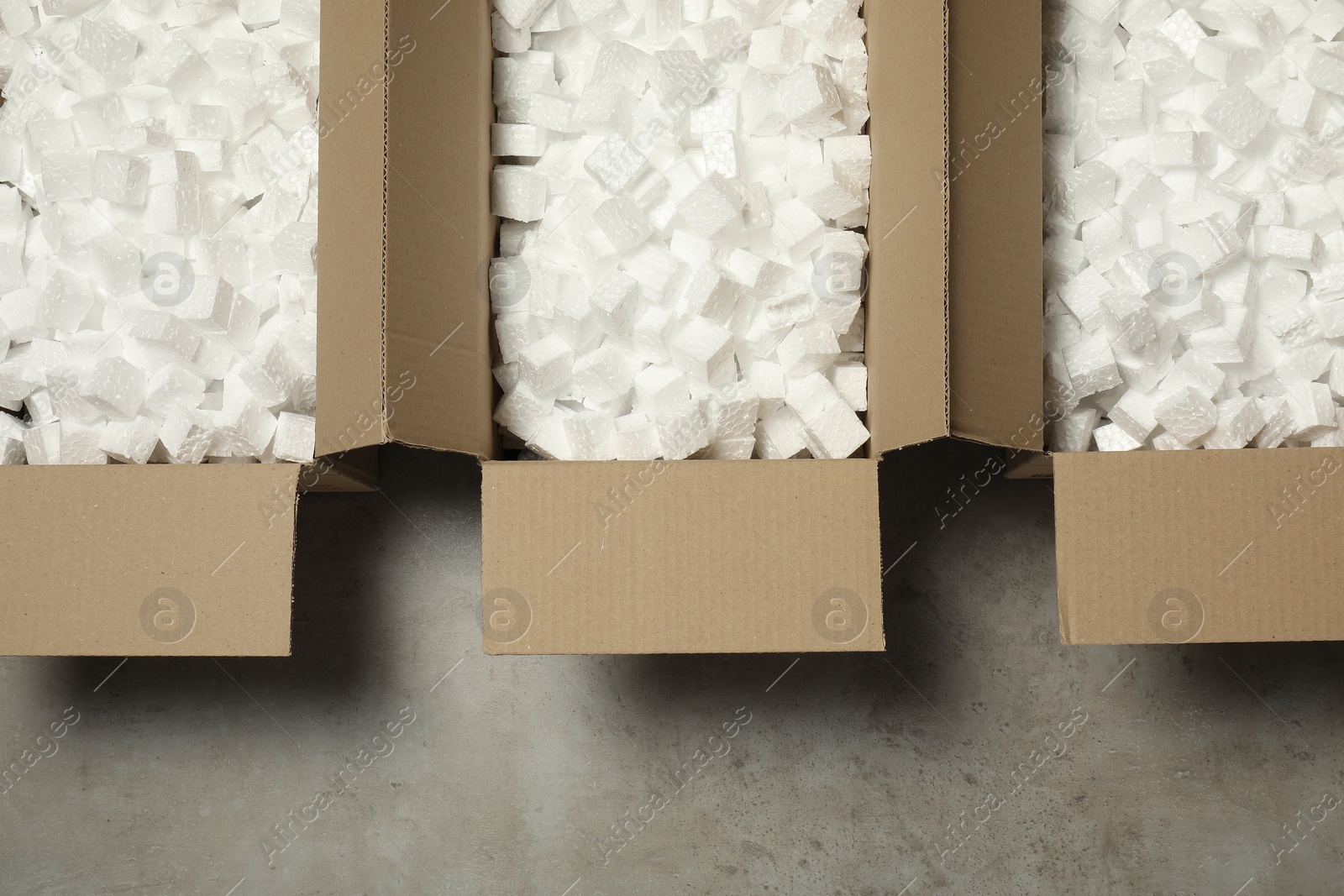 Photo of Many open cardboard boxes with pieces of polystyrene foam on grey floor, flat lay