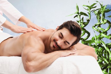 Image of Handsome young man receiving back massage in spa salon. Green bamboo stems on background
