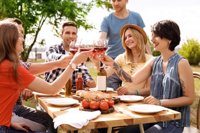 Photo of Young people with glasses of wine at table outdoors. Summer barbecue