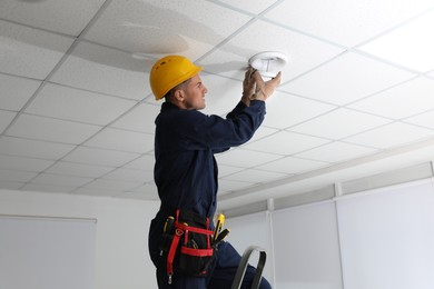 Photo of Electrician in uniform repairing ceiling lamp indoors