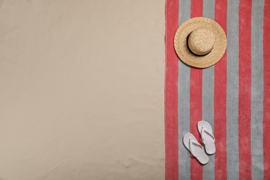 Beach towel, flip flops and hat on sand, top view. Space for text