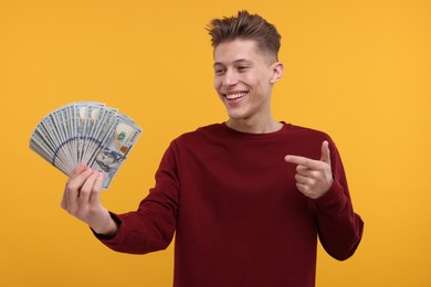 Photo of Happy man pointing at dollar banknotes on yellow background