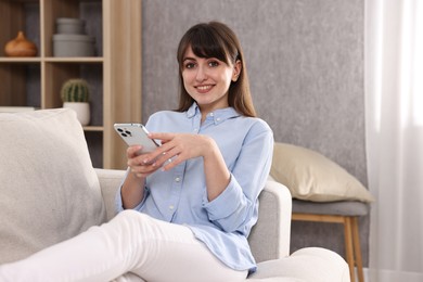 Photo of Beautiful young housewife using smartphone on sofa at home