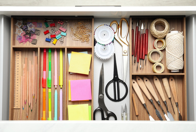 Sewing accessories and stationery in open desk drawer, top view