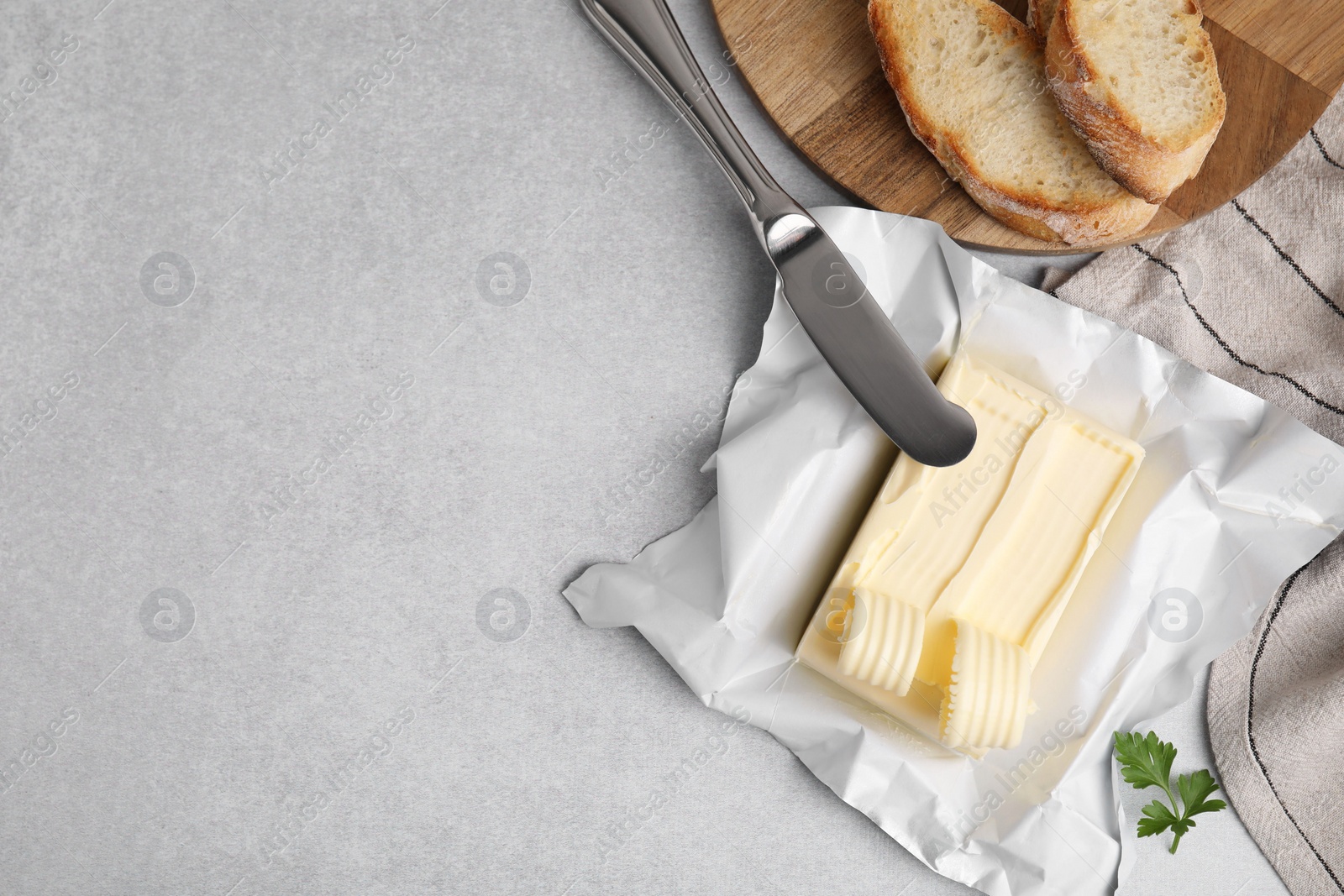 Photo of Tasty butter with curls, slices of bread and knife on light grey table, flat lay. Space for text