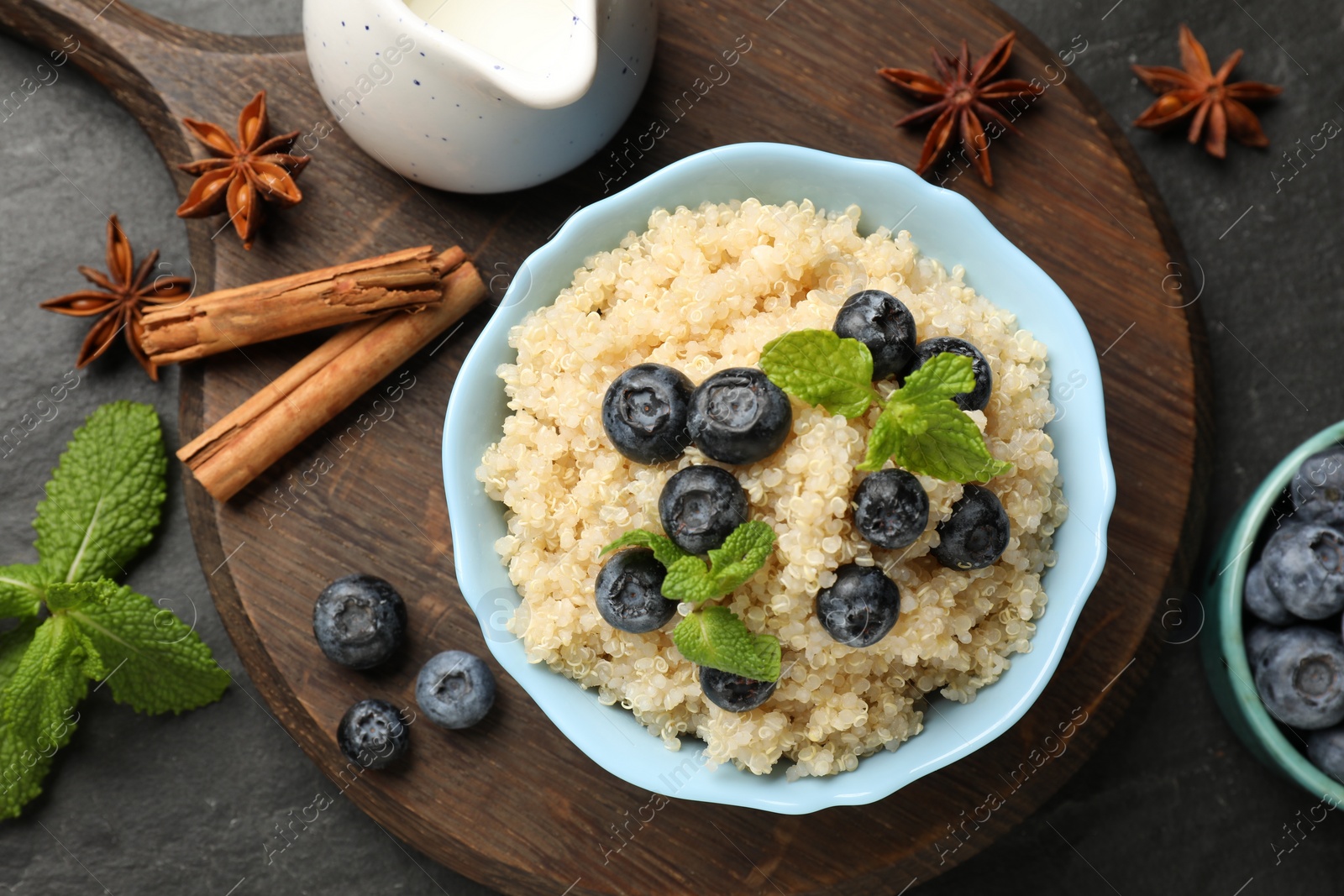 Photo of Flat lay composition with bowl of tasty quinoa porridge, blueberries and mint on black textured table