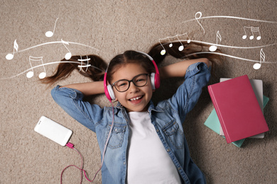 Cute little girl listening to music through headphones on floor, top view