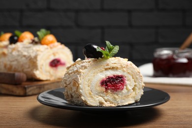 Photo of Slice of tasty meringue roll with jam, tangerine slices and mint leaves on wooden table